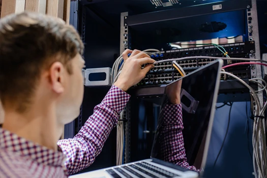 Person working on a Network switch thats inside a serverrack while holding a laptop in the other hand